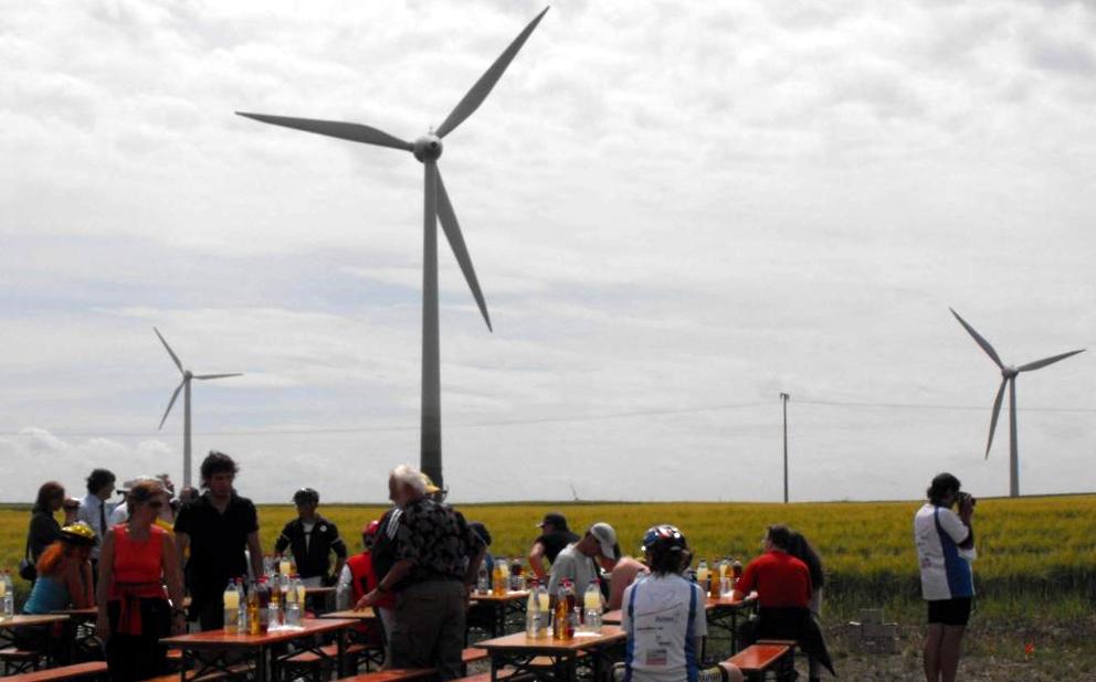 Landschaft mit Windkraftanlagen. Vorn rastet Bike for Peace and New Energies an gedeckten Tischen.